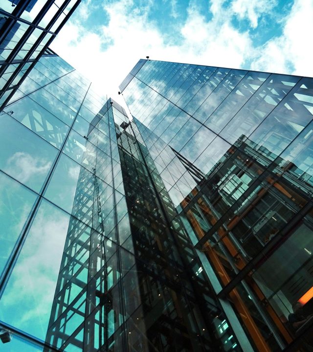 A striking view of a modern glass skyscraper reflecting the sky and clouds.